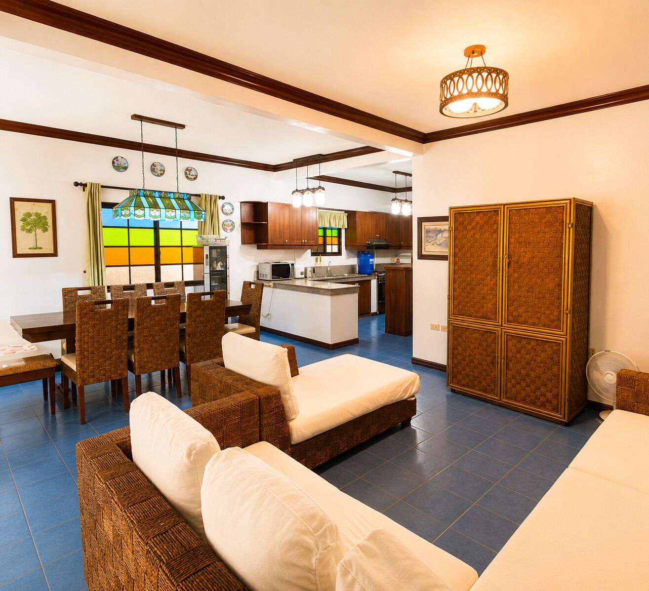 A living room with a sofa, dining area with chairs, kitchen with cabinets, and a fan.