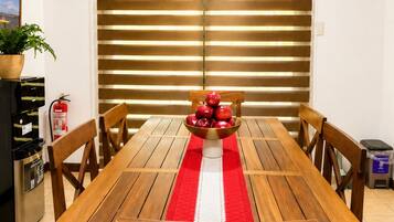 Un comedor con una mesa de madera, sillas, camino de mesa rojo y blanco, y un cuenco de manzanas.