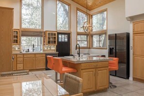 A spacious kitchen with wooden cabinets, a central island with seating, large windows, and a stainless steel refrigerator. - Powder and Pines on Knight, walk to the village (Big Bear Lake)