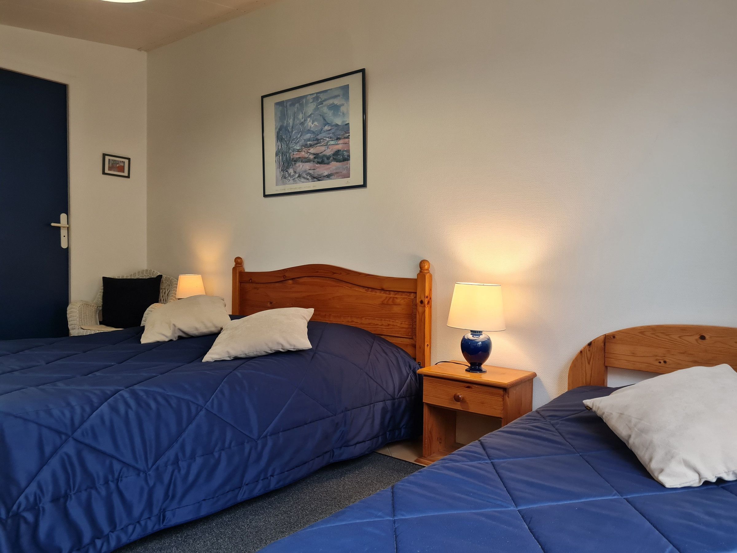 Un dormitorio con dos camas, un cabecero de madera, una mesita de noche con una lámpara y un cuadro enmarcado en la pared.
