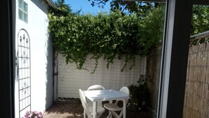 Un patio con una mesa y sillas blancas, una cerca blanca y un jardín con flores rosadas.