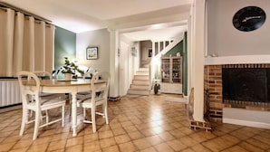 Un comedor con una mesa y sillas de madera, una escalera que sube a otro nivel y una chimenea.