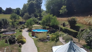 A backyard with a swimming pool, trampoline, and a tent.