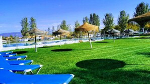 A poolside area with blue lounge chairs, a grassy lawn, and thatched-roof structures. - Bungalow with Terrace - Sleeps 2 (Humilladero)