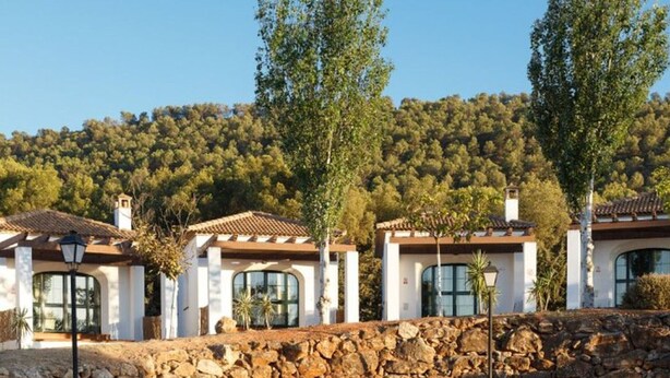 A row of Mediterranean-style villas with stone walls and tiled roofs, set against a backdrop of dense forest. - Bungalow with Terrace - Sleeps 2 (Humilladero)