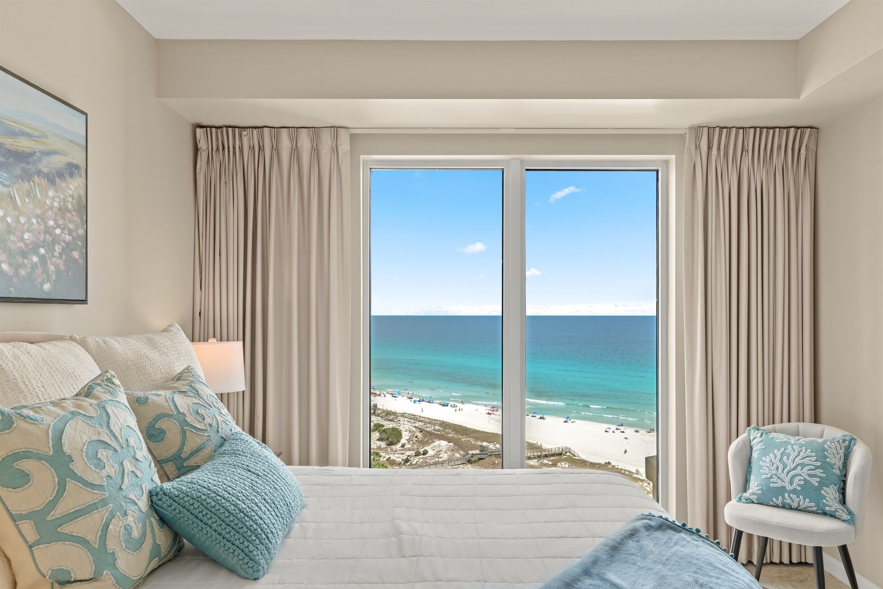 A hotel room with a large bed, a chair, and a view of the beach.
