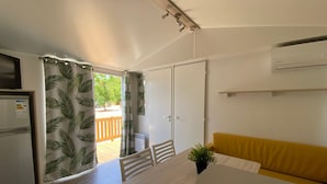 Ett kompakt kök med ett kylskåp, ett matbord med stolar, en gul soffa och en skjutdörr som leder ut till ett utomhusområde.