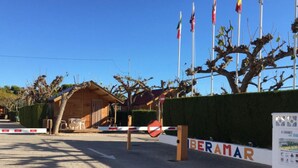 Un edificio con fachada de madera, entrada protegida por una reja y banderas al fondo.