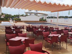 An outdoor dining area with red chairs and tables, a pool, and a water slide in the background.