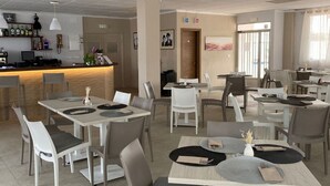 Un restaurante moderno con mesas y sillas blancas y grises, una zona de bar con botellas y cuadros en las paredes.