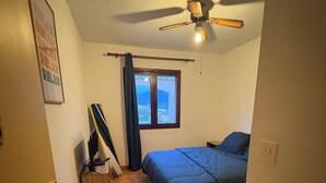 Quarto com cama, ventilador de teto, janela com cortinas e porta.