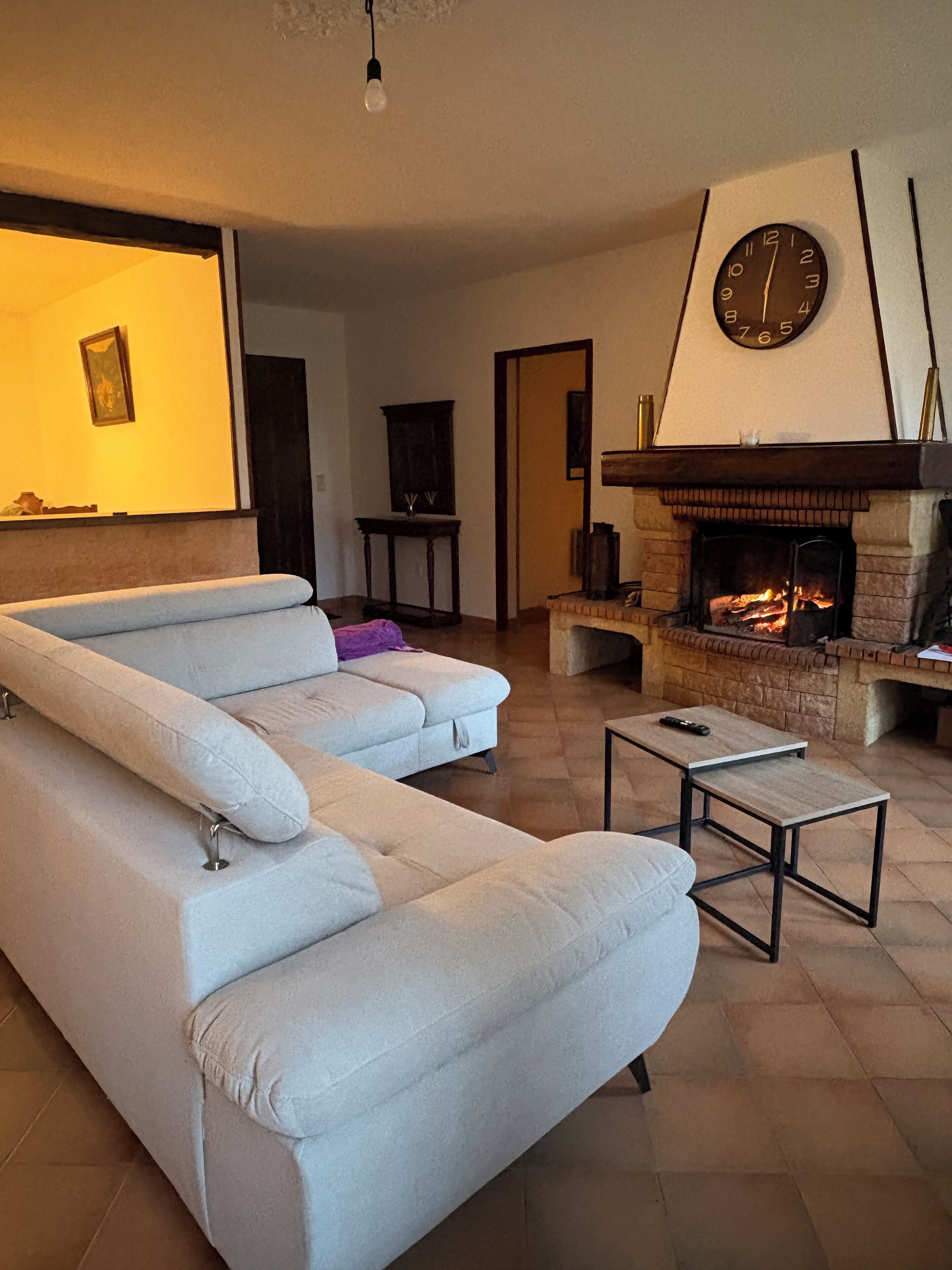 Un salon avec un canapé d’angle, une cheminée et une horloge au mur.