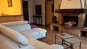 Uma sala de estar com sofá seccional, lareira e relógio na parede.