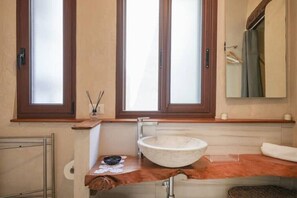 Une salle de bain avec une grande fenêtre, un meuble-lavabo en bois, un lavabo blanc et un porte-serviettes.