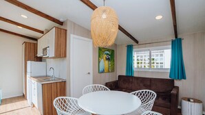 A compact living space with a kitchenette, a dining area with white chairs, a brown sofa, and a large woven light fixture. - Mobile Home with Terrace in Crevillent (Crevillente)