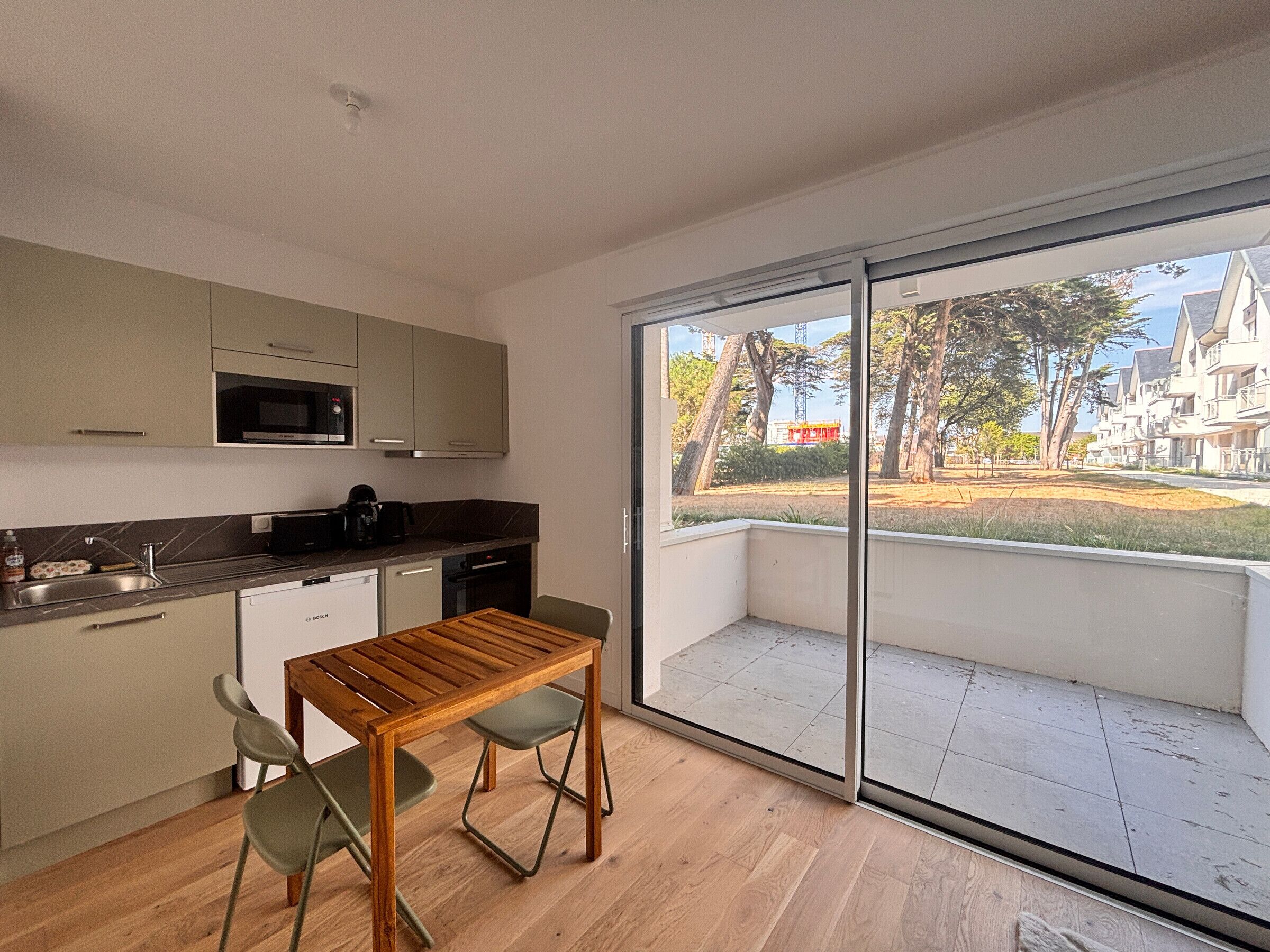 A modern kitchen with a dining area, large sliding glass doors, and a view of a residential area.