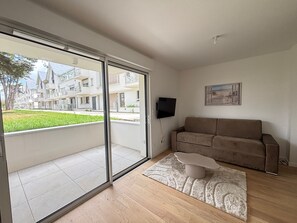 A modern living room with a sliding glass door, a flat-screen TV, a beige sofa, and a patterned rug. - Studio for 2 with terrace and parking in new building (Les Sables-d'Olonne)