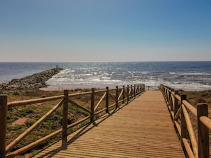 Une promenade en bois mène à une côte rocheuse où les vagues se brisent sur la plage.