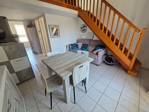 Ein Essbereich mit Holztisch und Stühlen, einer Couch mit Kissen, einer Treppe und einer Wanduhr.
