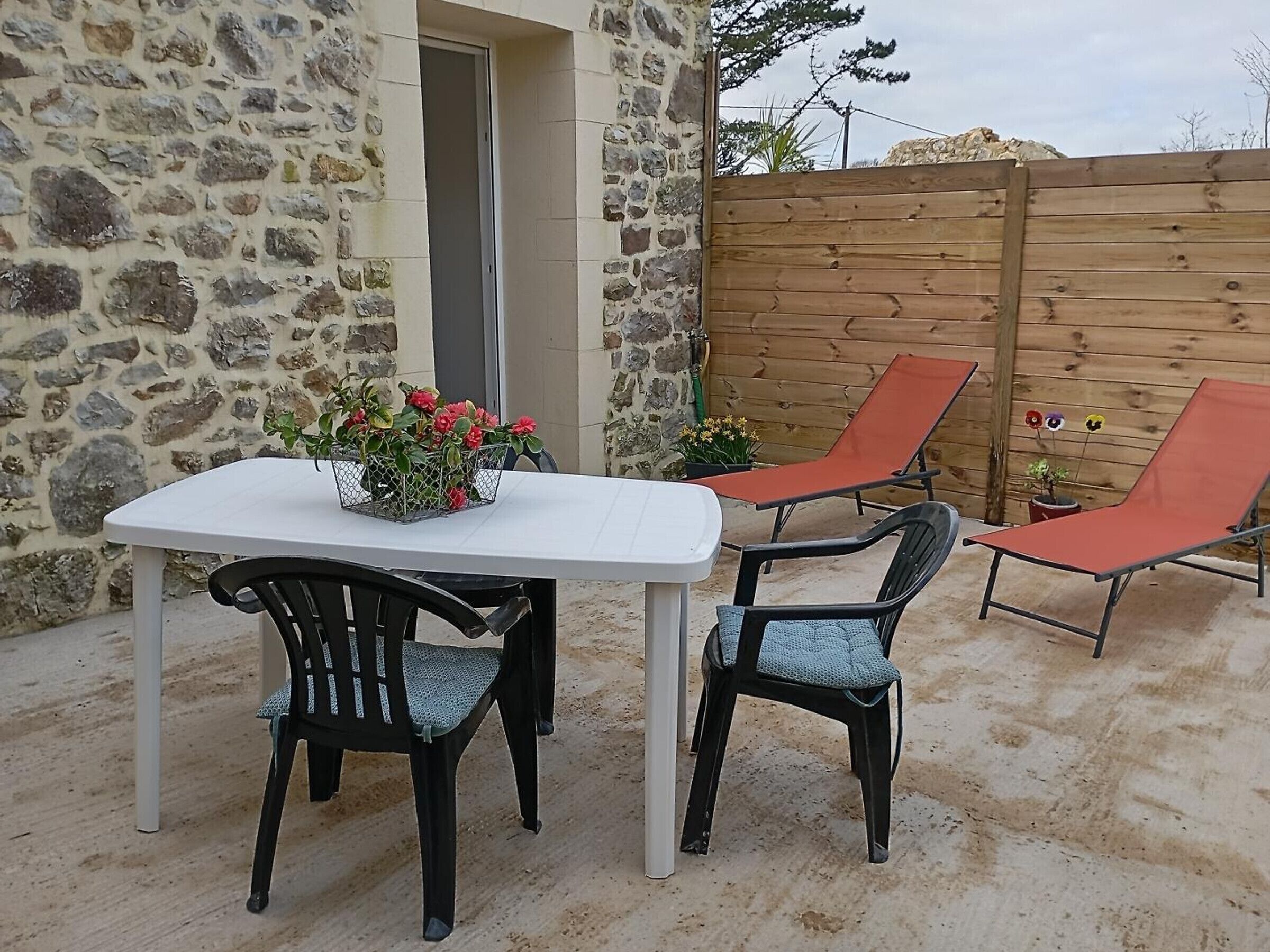 An outdoor patio with a stone wall, a wooden fence, and a table with chairs.