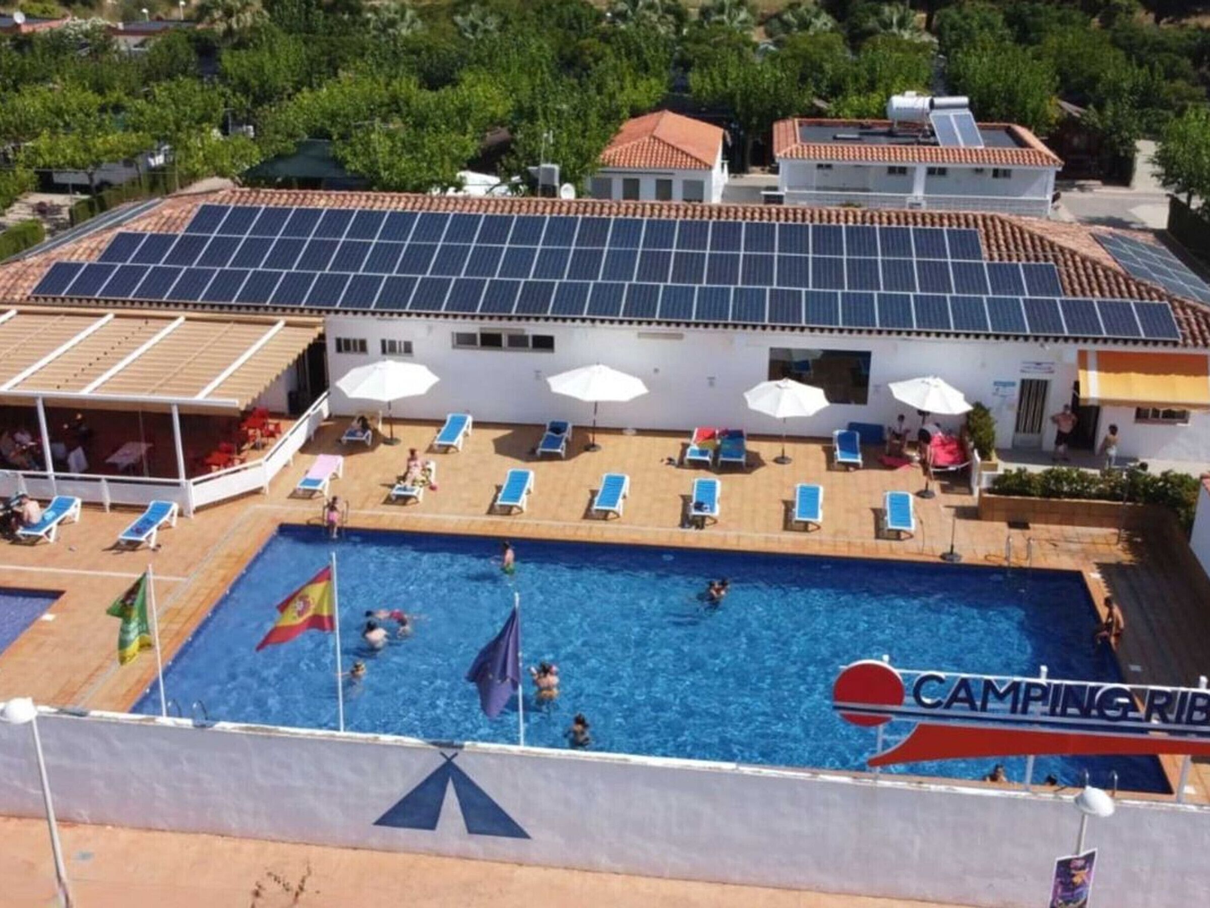 En pool på taket med solpaneler, solstolar och en flagga.