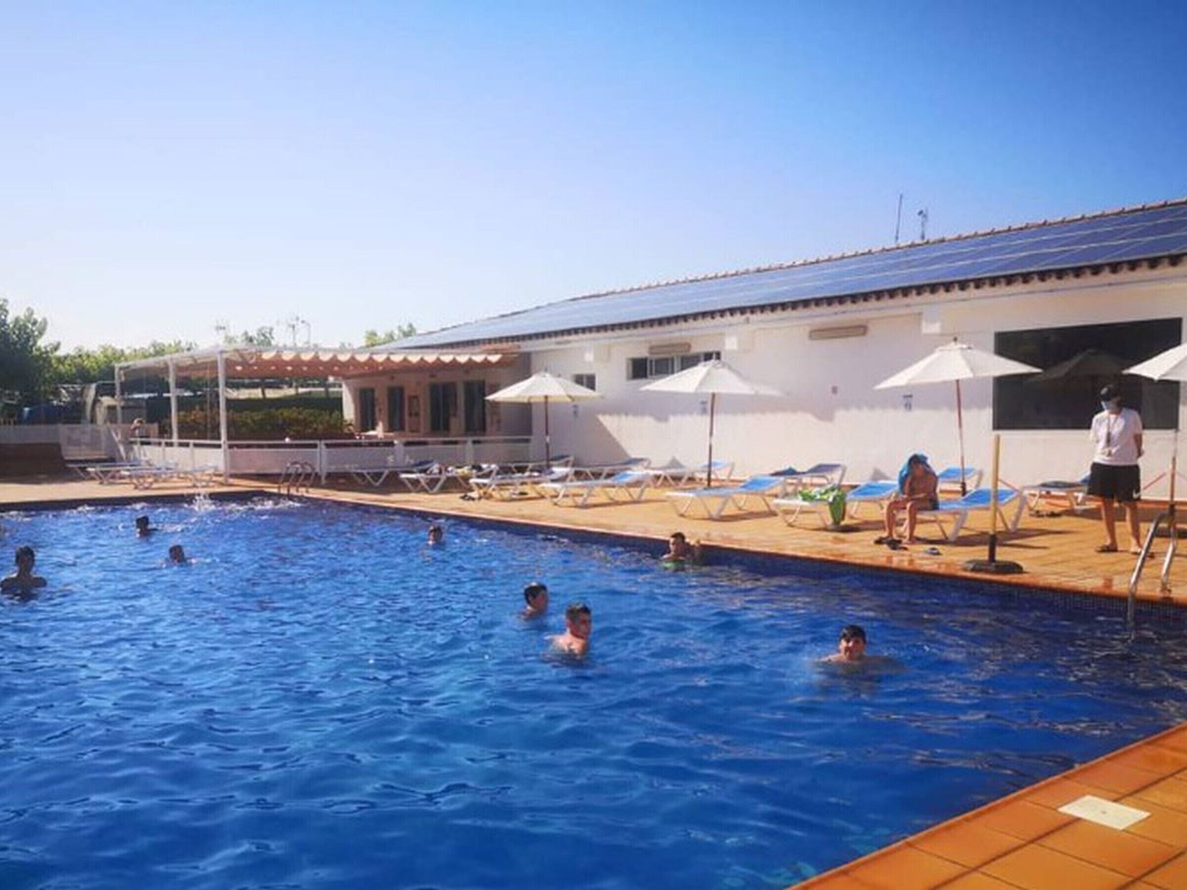 A swimming pool with people swimming and lounging under umbrellas.