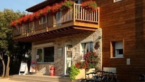 Een houten gebouw met een balkon versierd met rode bloemen, een stenen gevel en een fiets voor de deur.
