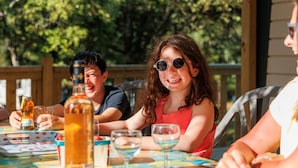Een groep mensen zit aan een buitentafel met een kleurrijke tafelkleed, terwijl ze van drankjes en eten genieten.