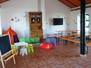 A classroom with wooden benches, a blackboard, colorful play mats, and a cabinet with glass doors.