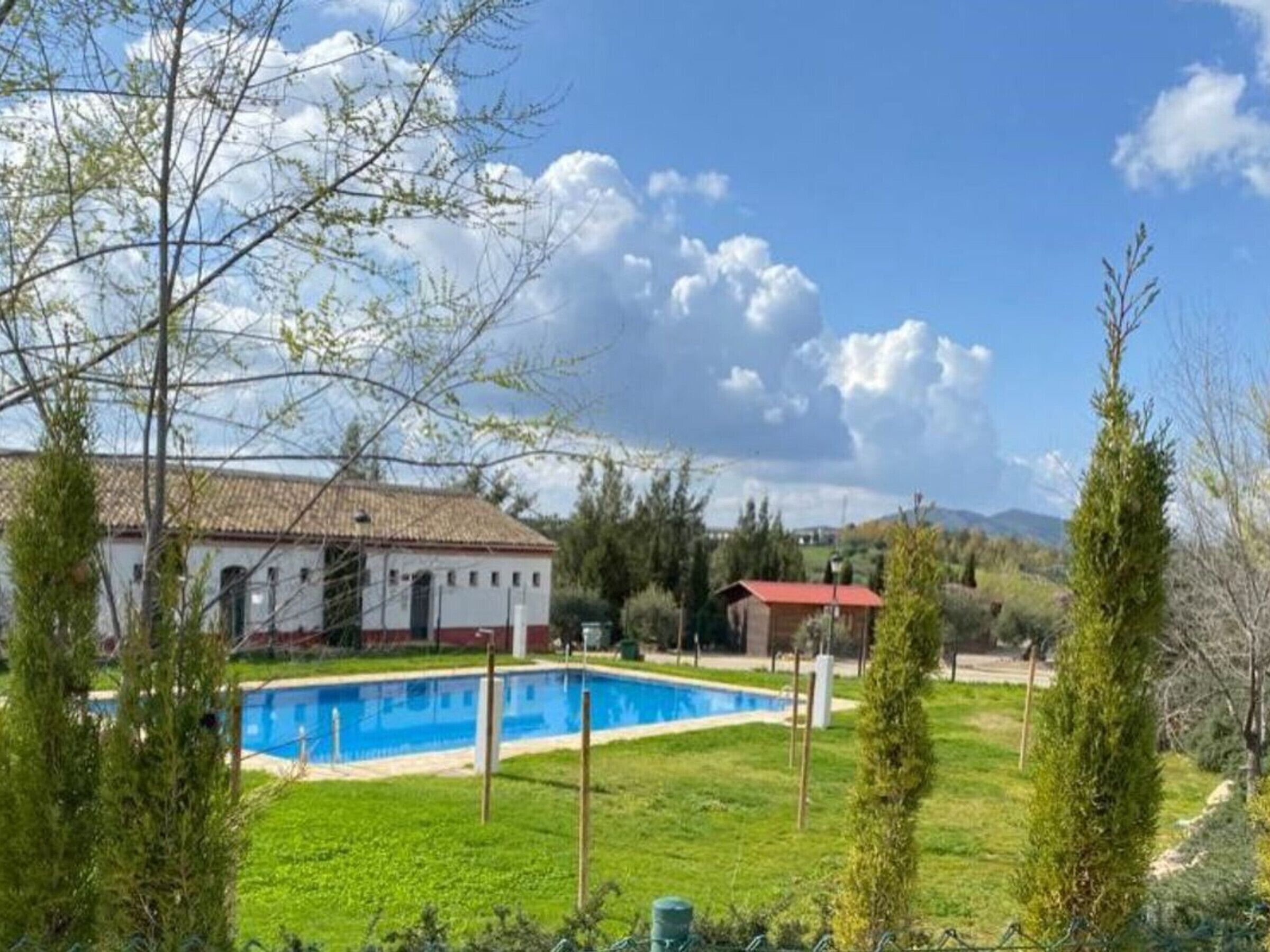 Una casa con piscina, rodeada de vegetación y cielo despejado.