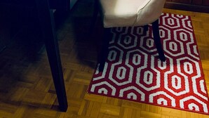 A room with a wooden paneled wall, a white table, a cushioned chair, a framed picture, a desk lamp, and a patterned rug. - yonge & finch subway cozy rooms for rent (Toronto)