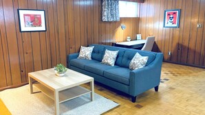 A living room with a blue sofa, a wooden coffee table, and a small plant. There are two framed pictures on the walls and a window with curtains. - yonge & finch subway cozy rooms for rent (Toronto)
