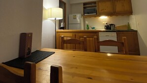 Una cuina compacta amb armaris de fusta, microones, nevera i taula de menjador amb caires.