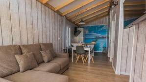 A cozy living area with a sofa, dining table, and chairs. A kitchen is visible in the background with a view of the sea through a window. - Bungalow with Terrace and Accessible Ramp in Guardamar (Guardamar del Segura)