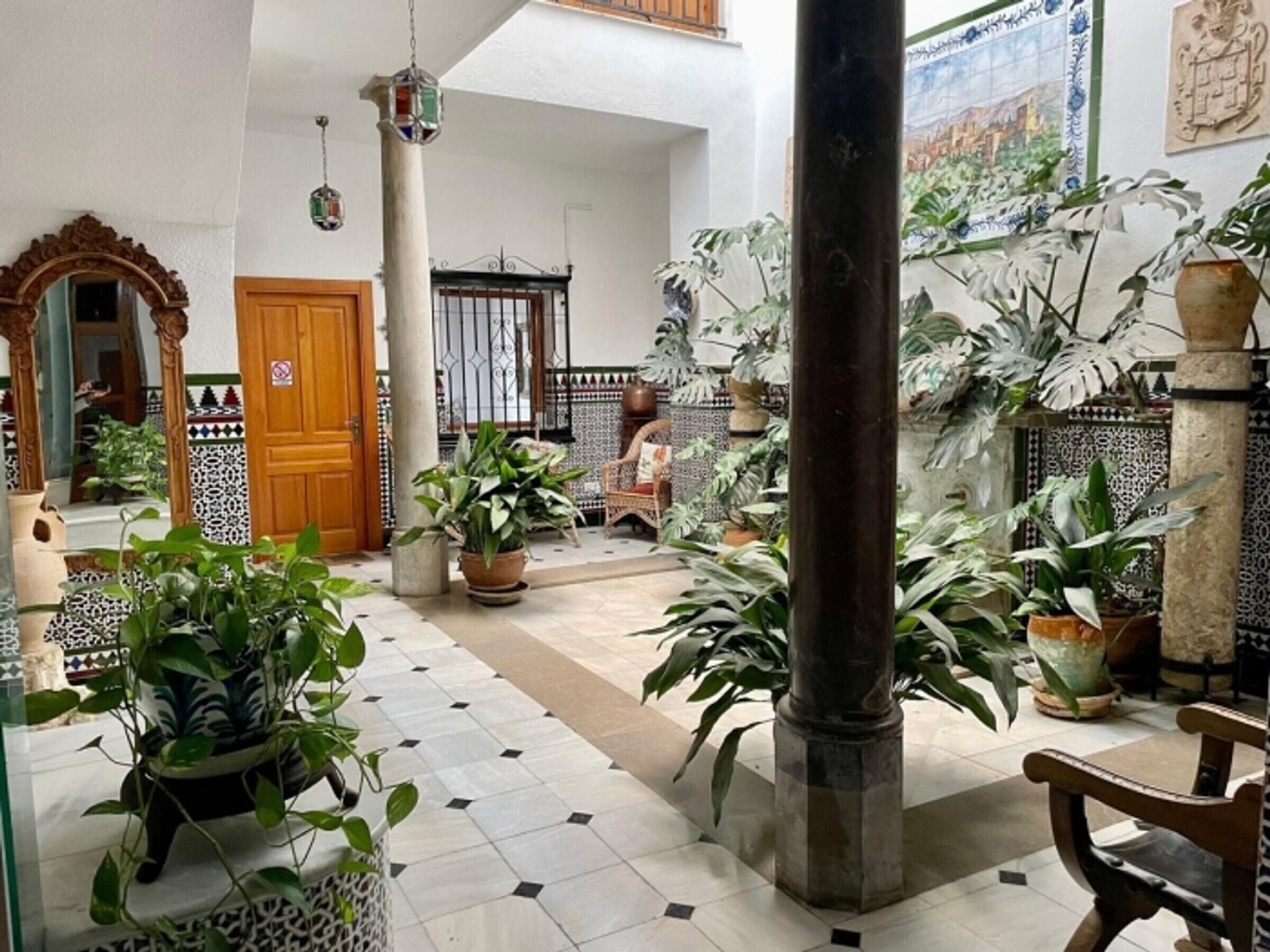 A spacious courtyard with tiled flooring, potted plants, a wooden bench, and a large column.