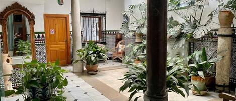 A spacious courtyard with tiled flooring, potted plants, a wooden bench, and a large column.