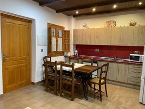 A kitchen with wooden cabinets, a dining table with chairs, a microwave, and a clock on the wall. - Charming 18th-century home in Granada, parking included (Granada)