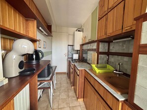 A compact kitchen with wooden cabinets, a coffee maker, a sink, and a small dining area. - Air-Conditioned T2 Apartment for 4 in Argelès-sur-Mer with Parking (Argelès-sur-Mer)