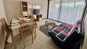 Un salon avec une table à manger dressée pour deux personnes, un canapé, un téléviseur posé sur un meuble et une fenêtre avec des rideaux.