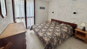 Une chambre à coucher avec un lit, un bureau, une chaise, une table de chevet et une fenêtre avec des rideaux.