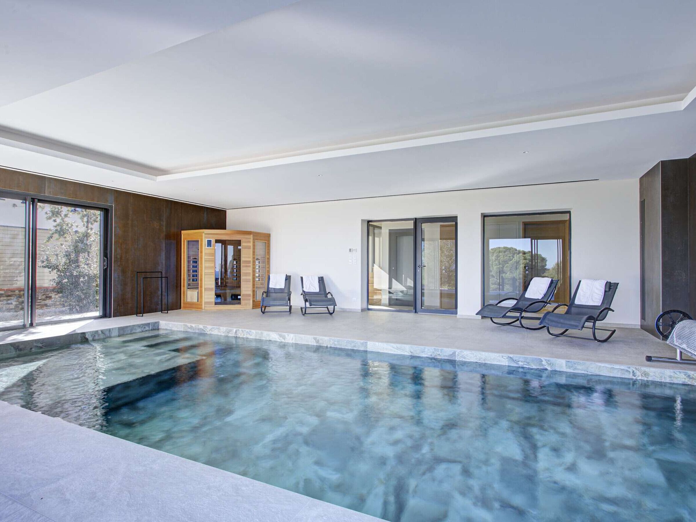 A modern indoor pool with clear water, surrounded by lounge chairs and a sauna area.