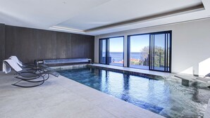 Ein moderner Innenpool mit Meerblick, einer Sitzgruppe und einem Liegestuhl.