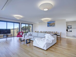 A modern living room with a large sofa, a red chair, a coffee table, and a TV. There are large windows offering a view of the outdoors. - Exclusive Villa in Banyuls-sur-Mer - Comfort & Luxe (Banyuls-sur-Mer)