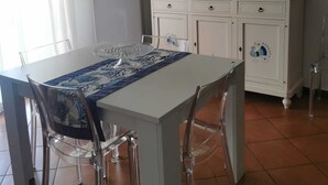 A kitchen with a dining table, chairs, a refrigerator, a cabinet, and wall art. - Apartment Le Pavoncelle Lido ideal for Families (Alghero)