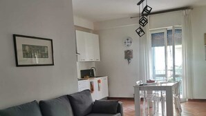 Un salon avec un canapé gris, une petite table et un coin repas comprenant une table et des chaises blanches.