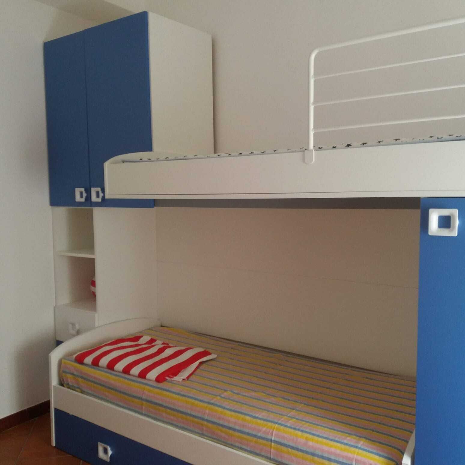 Un lit superposé avec un lit supérieur blanc et un lit inférieur doté d’un matelas à rayures. On trouve une armoire bleue au-dessus du lit inférieur.