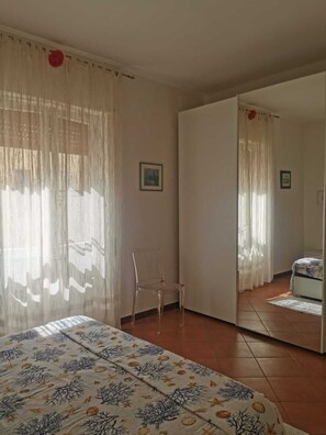 A bedroom with a bed, a chair, a wardrobe, and a mirror. - Apartment Le Pavoncelle Lido ideal for Families (Alghero)