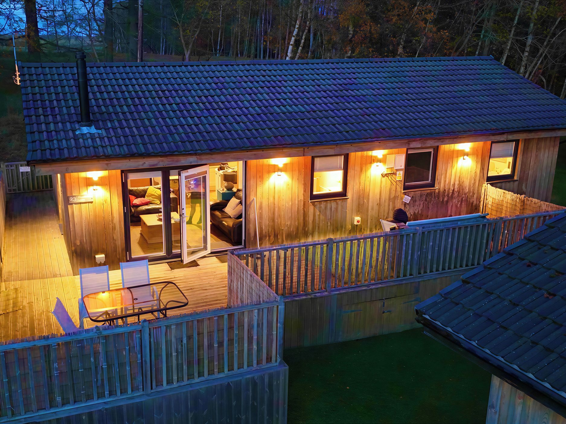 A wooden cabin with a deck, a covered porch, and a single visible room with a bed and a chair.