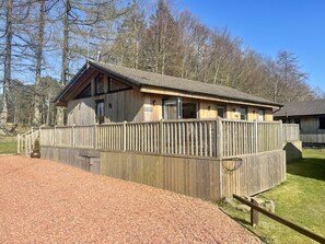 A wooden cabin with a fenced deck, surrounded by trees. - Woodburn Lodge (Newcastle-upon-Tyne)