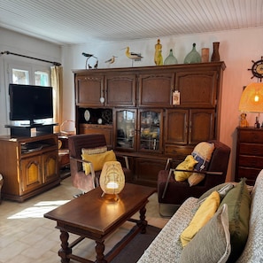 A living room with a television, wooden furniture, a lamp, and decorative items on the wall. - La Maison du Pecheur - Premiere Conciergerie (Palavas-les-Flots)